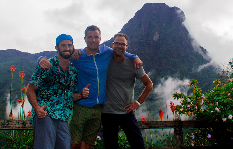 Three tourists smiling in front of a mountain and flowers