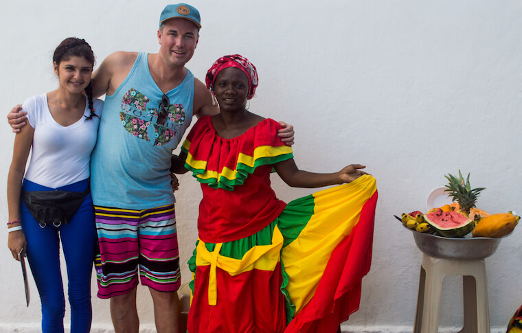 Two tourists and a woman in colorful traditional Colombian clothing